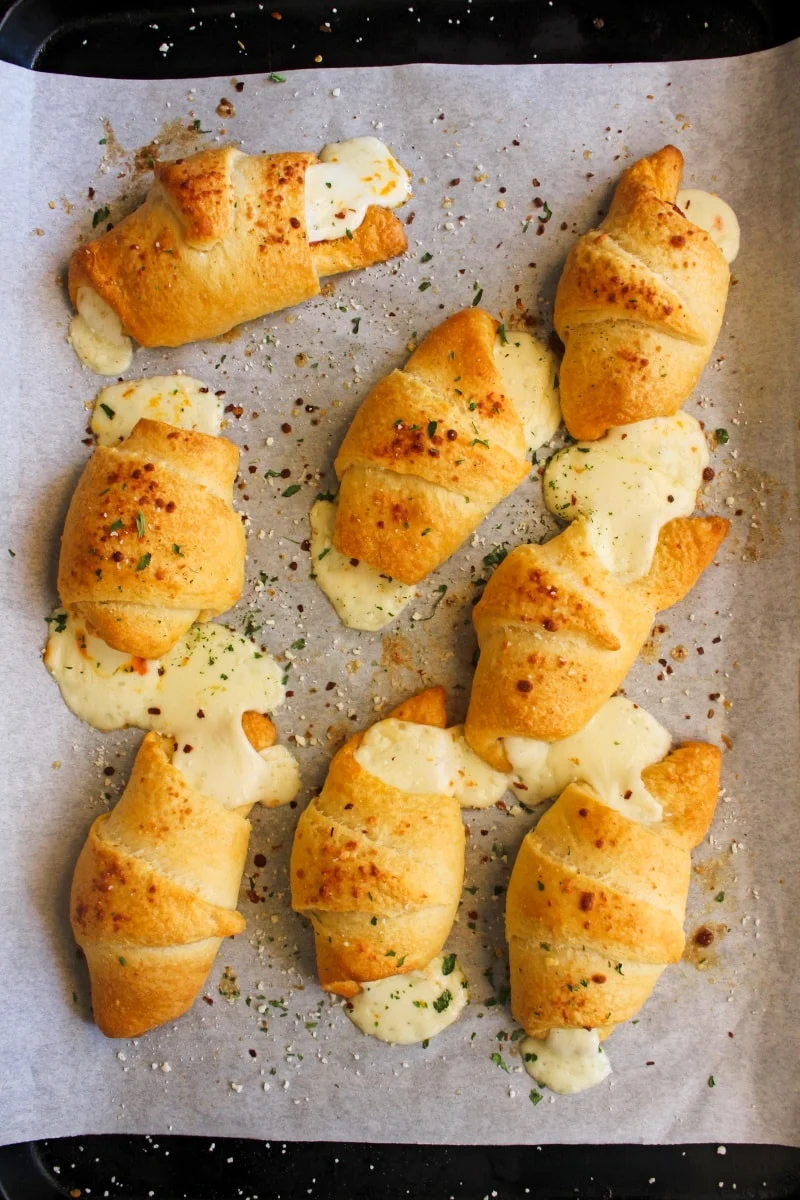 Top view of eight pizza crescent rolls on a parchment-lined baking sheet.