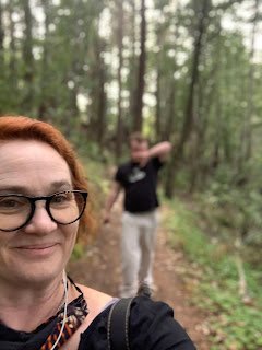 Selfie of me on a redwood trail  Leo is visible, blurrily, behind me.