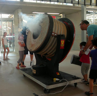 A parent helps a child hold the mallet to hit the diaphragm of the smoke cannon.