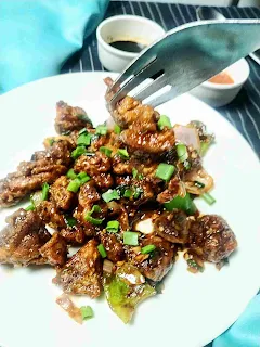 Serving chicken manchurian with a fork, chilly and soya sauce in background