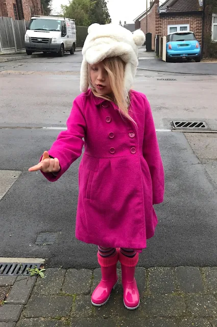 A 5 year old girl standing on a residential street with her hand out trying to catch a snowflake on her finger