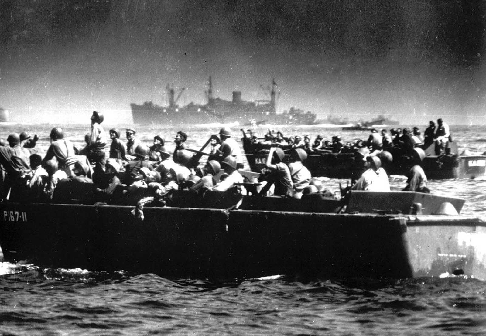 Landing barges loaded with U.S. troops bound for the beaches of Leyte island, in October 1944, as American and Japanese fighter planes duel to the death overhead. The men aboard the crafts watch the dramatic battle in the sky as they approach the shore.