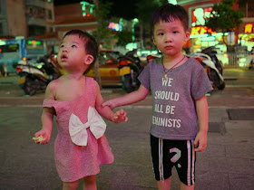 a child wearing a "We should all be feminists" shirt holding the arm of a child wearing a dress with a large white bow 