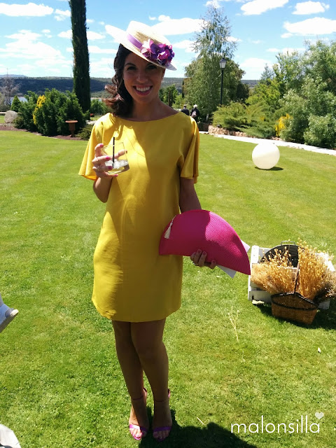 Invitada boda con vestido amarillo mostaza de Zara, sandalias lila, bolso abanico fucsia y canotier de copa baja en color malva y rosa