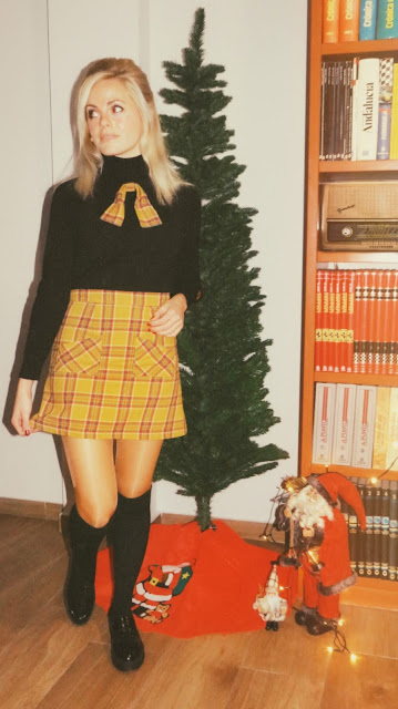 Alejandra Colomera con falda de cuadros mostaza, lazada a juego, jersey negro y abrigo estilo sesentero