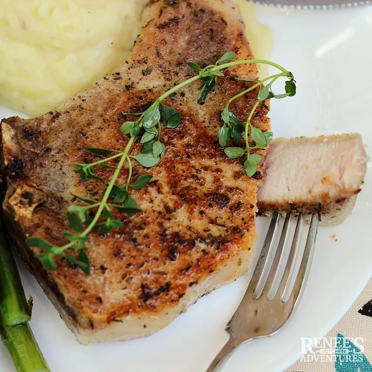 Close up of browned sous vide pork chop with thyme on it and a piece cut off ready to eat