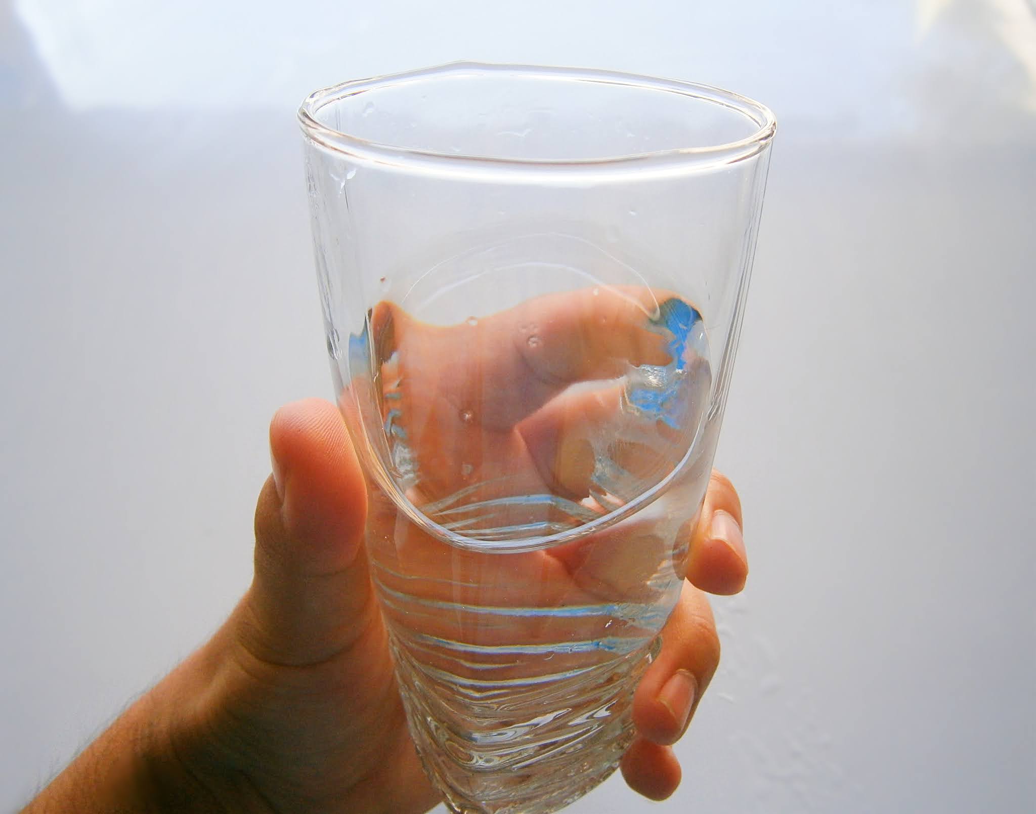 Vaso de agua fresca sostenida de una mano de una persona joven