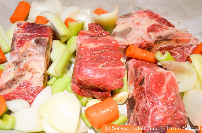 5 Pounds meaty beef neck bones with onions, carrots, garlic, and celery on a rimmed baking sheet.