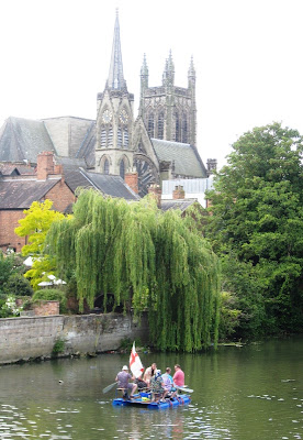 Raft on river with weeping willow and church tower in the background