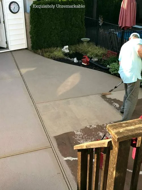 A man painting a cement patio with a roller.