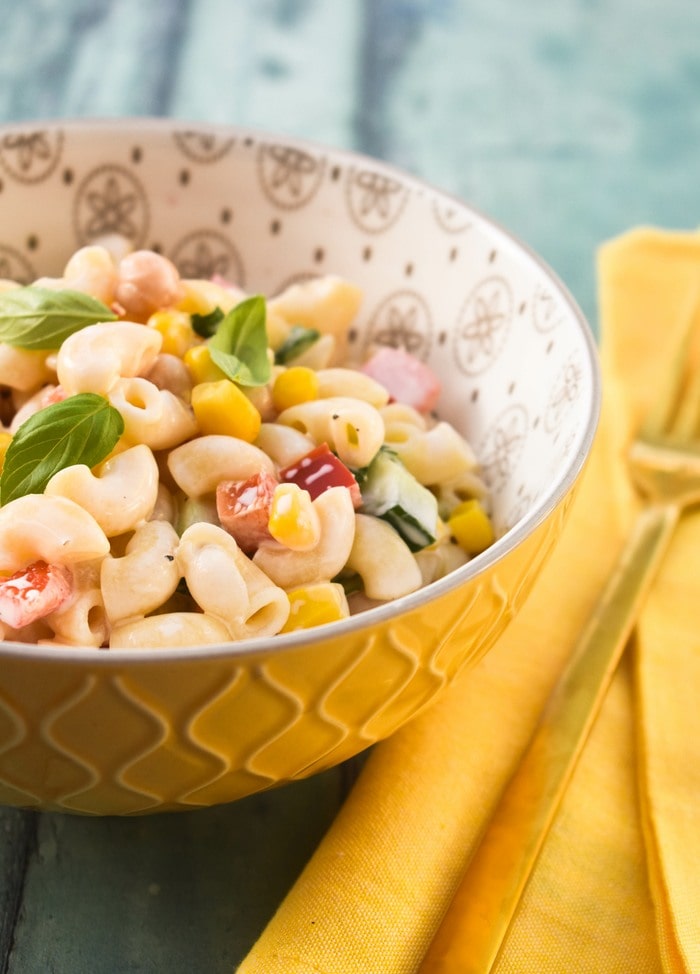 Macaroni salad in a floral bowl next to a yellow linen napkin topped with a gold fork