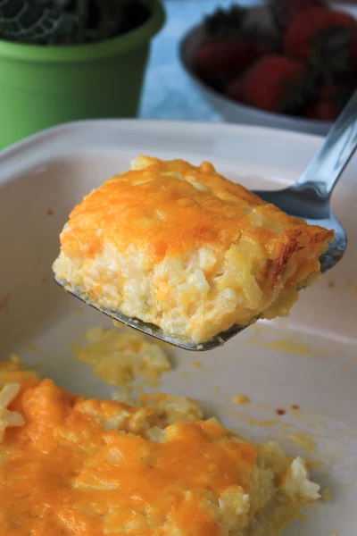A side view of a spatula serving a sqaure of hash brown casserole.