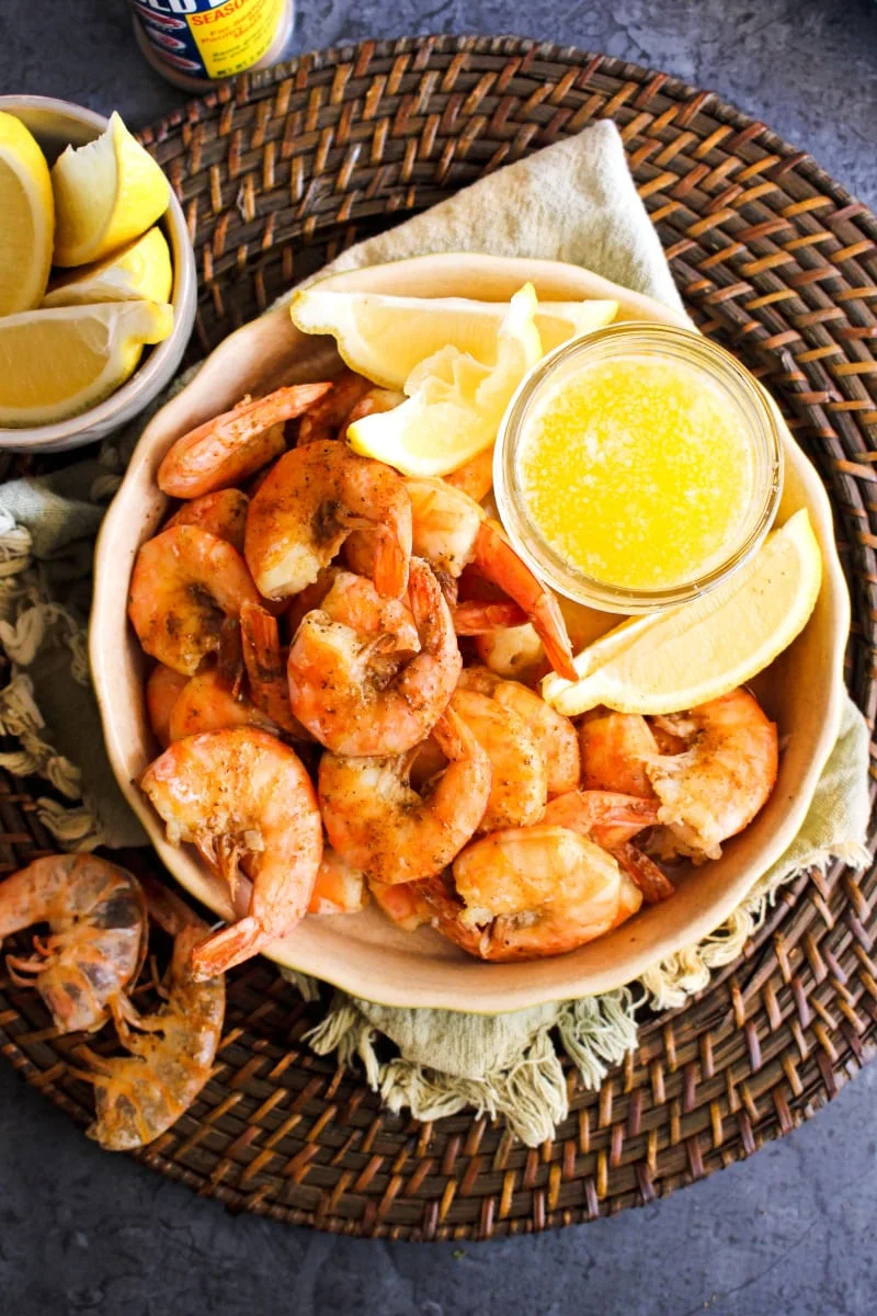 Air Fryer Peel and Eat Shrimp in a tan dish with lemons and drawn butter on the side.