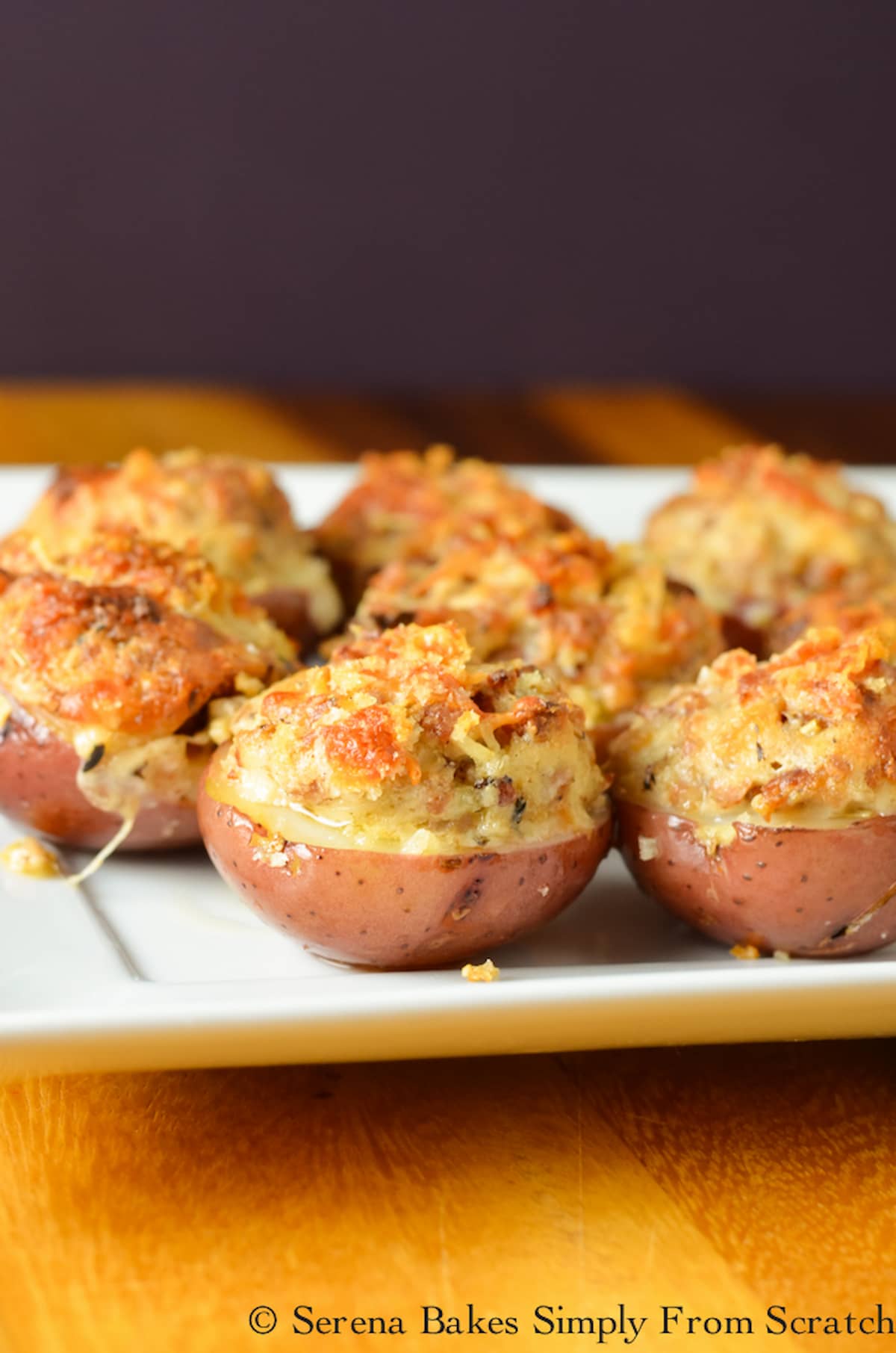 A side shot of Cheesy Sausage Stuffed Red Potatoes on a white tray that is on top of a wooden cutting board.