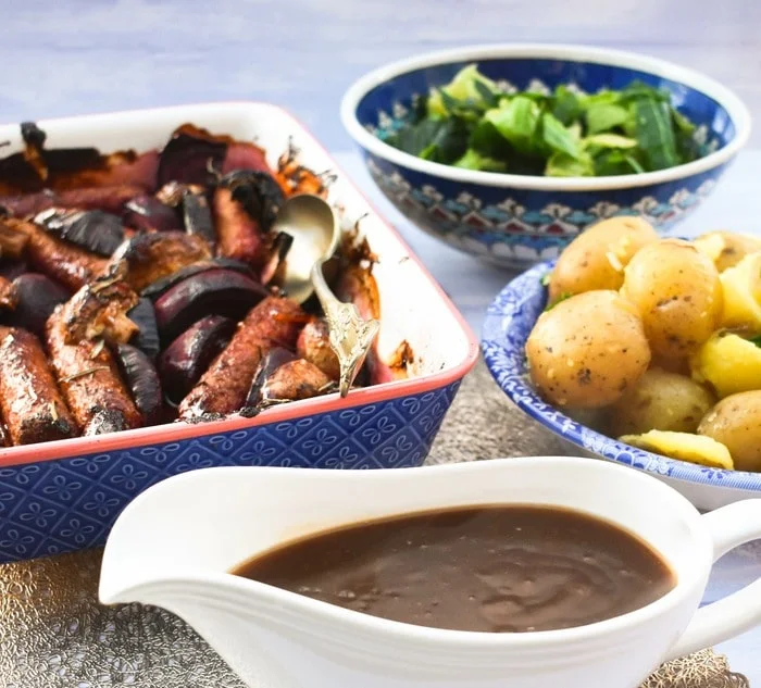 sticky sausage bake, bowl of potatoes, bowl if cabbage & a jug of gravy