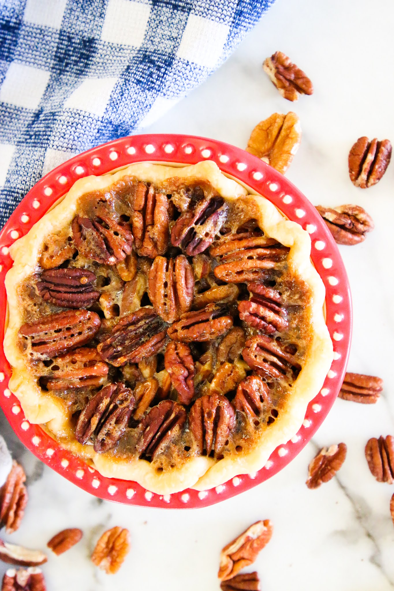 Pecan pie in a red pie dish with a blue dish towel in the background.