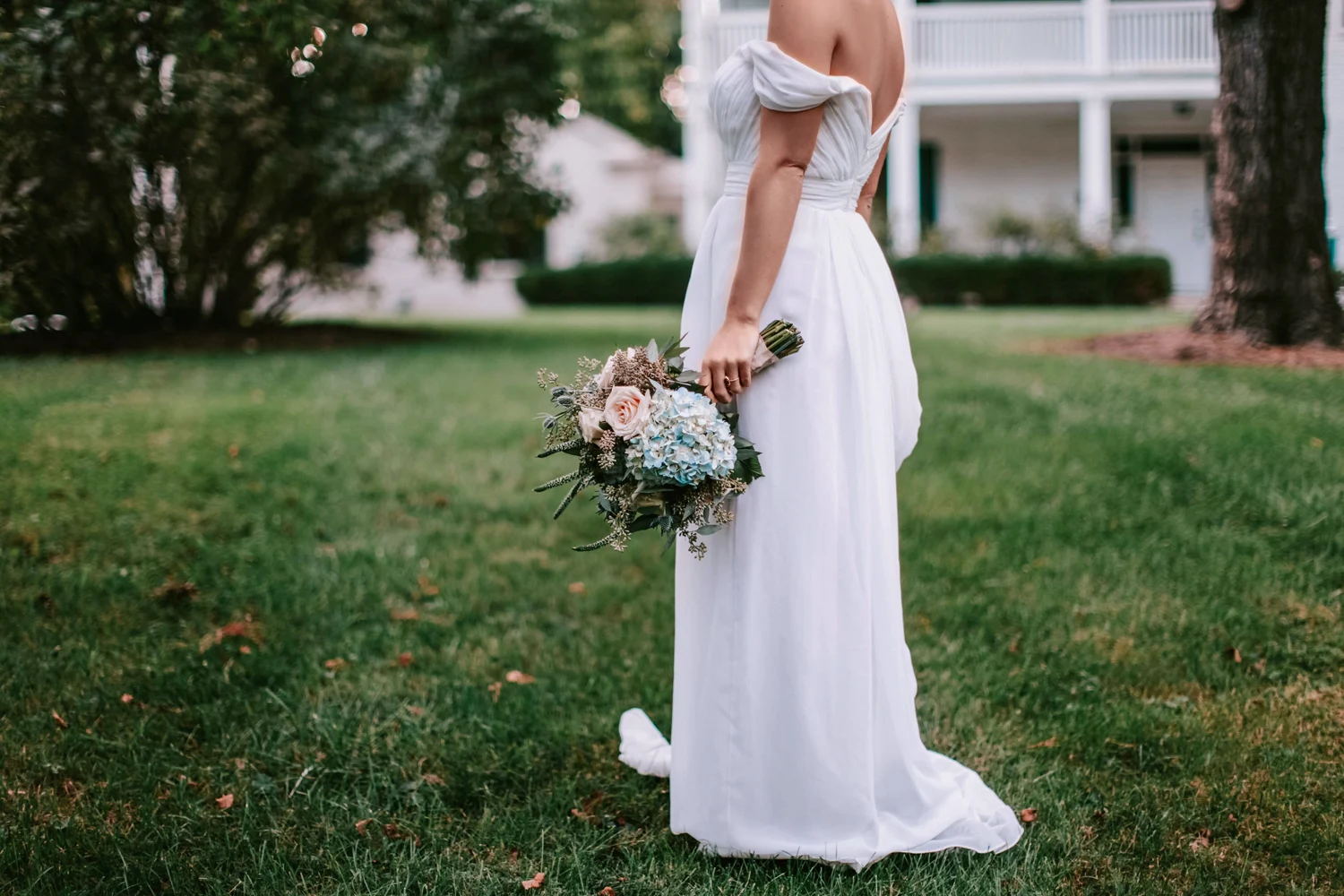 bride in a long dress holding bouquete and posing on the grass