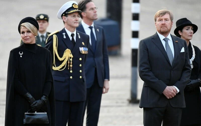 Queen Maxima wore a black wool high collar cape coat. Black leather handbag. Pearl drop earrings and diamond brooch. Gripoix earrings