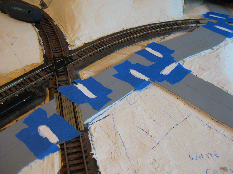 Stop lines masked out with masking tape and painted white on a plaster road