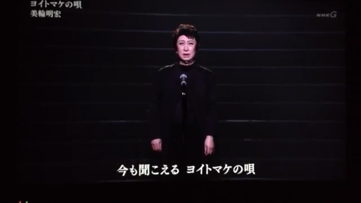 暗闇の中で男装して『ヨイトマケの唄』を歌う美輪明宏