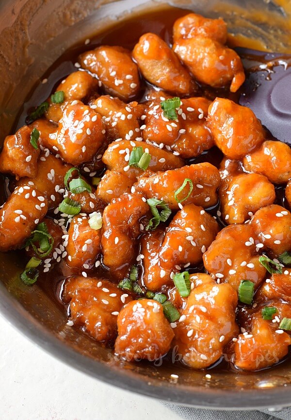 close up of sweet and sour chicken topped with sesame seeds and spring onion