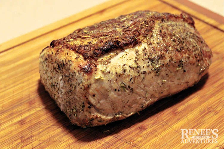 Finished pork ribeye roast resting on wood cutting board waiting to be sliced and served