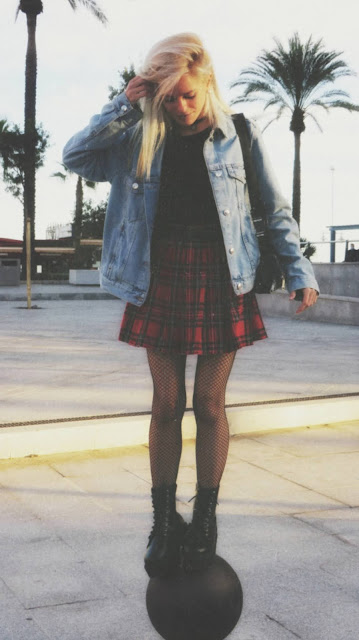 Estilo grunge con camiseta negra, falda de tablas tartán, medias de red grande, botas estilo militar y cazadora vaquera