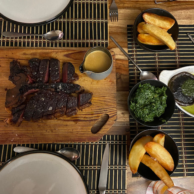 A steak carved up and lying on a wooden board, plus dishes of chips and creamed spinach.