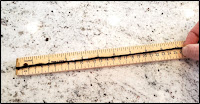 A hand holding a black yarn on top of a ruler measuring