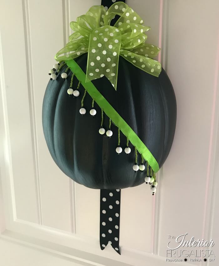 An easy peasy Halloween half pumpkin door hanger that won't scare trick or treaters made with craft pumpkins and assorted green and black ribbon.