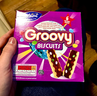 A purple square box with groovy biscuits in white thick font with a picture of a rectangular biscuit on it on a bright backgroun