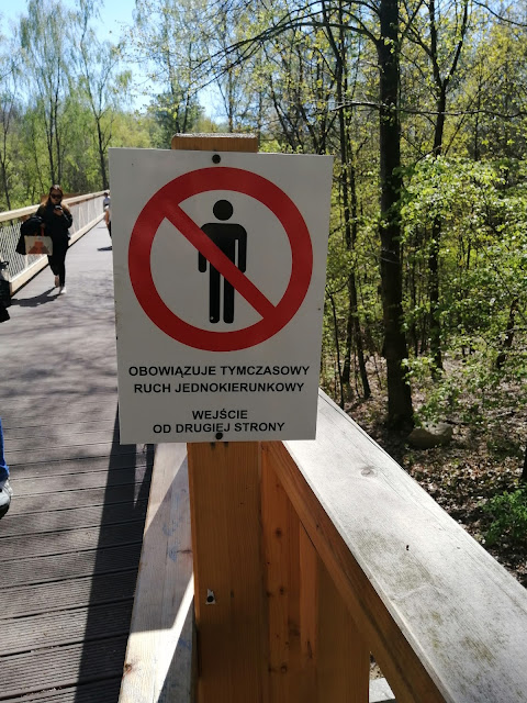 Na zdjęciu widać tabliczkę zawieszoną na drewnianej konstrukcji z oznaczeniem przedstawiającym zakaz ruchu pieszego