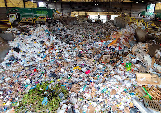 Garbage dumped across a concrete collection facility with a waste management truck in the background