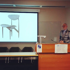 Geoff Isaac giving a talk in front of a slide of a Scape dining chair by Grant Featherston.