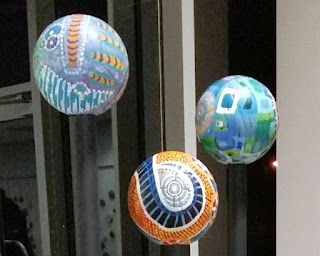 A closer view of the top three volleyballs which have abstract designs painted on them. Dominant colours and shapes include blues, greens, white, orange and purples, with stripes, dots, swirls and patches of colour.