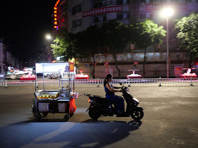 woman on motor scooter towing a food cart