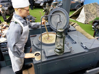 1/6 scale German soldier stirring soup in a diorama of an army post on display at a scale model exhibition.