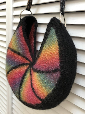 Felted bag knitted with rainbow colored and black yarn with icord handle attached with D rings