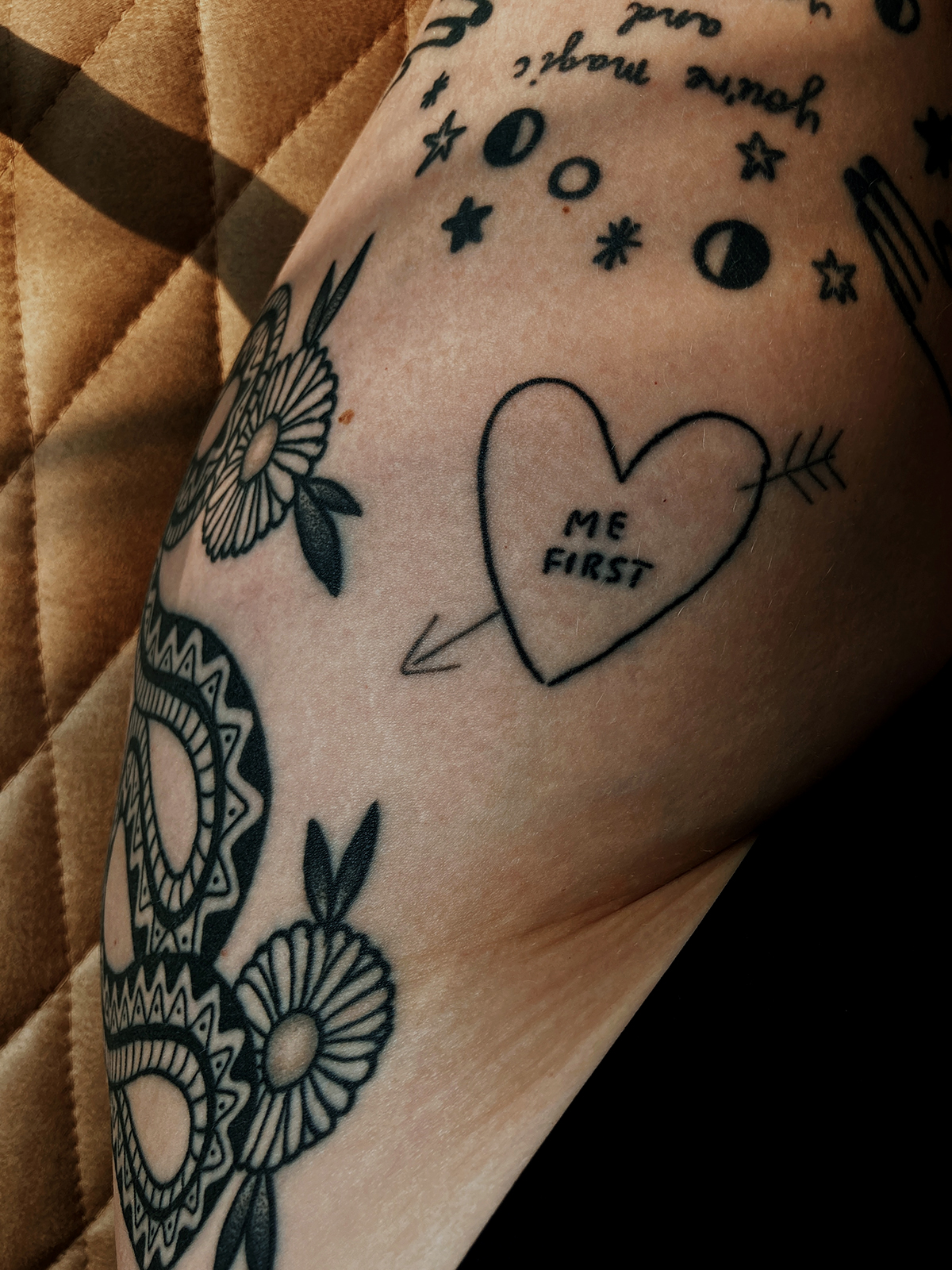 Close up of tattooed thigh, focusses on heart shaped tattoo that reads "me first".