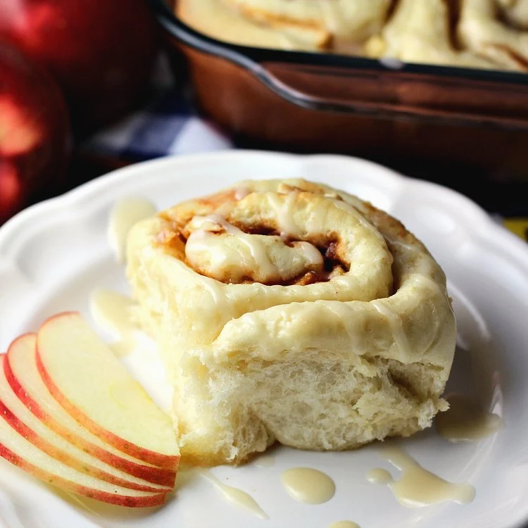 Apple Cinnamon Rolls with Maple Glaze on a white plate with slices of apples, ready to eat.