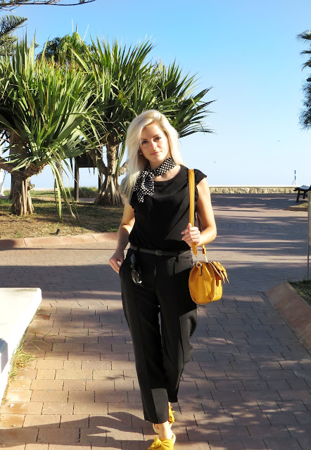 Alejandra Colomera con camiseta negra, pantalón formal negro, lazo en el cuello negro con lunares blancos y complementos mostaza