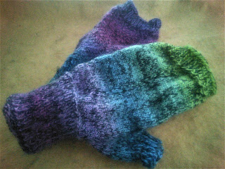 two fingerless mittens knit in a rainbow gradient marled with black. 