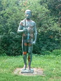 Statue, einst heroisch, jetzt mit Graffitti übersäht am Eingang vom Volkspark Friedrichshain.Muskulöser Mann mit einer Art Fackel in der Hand.