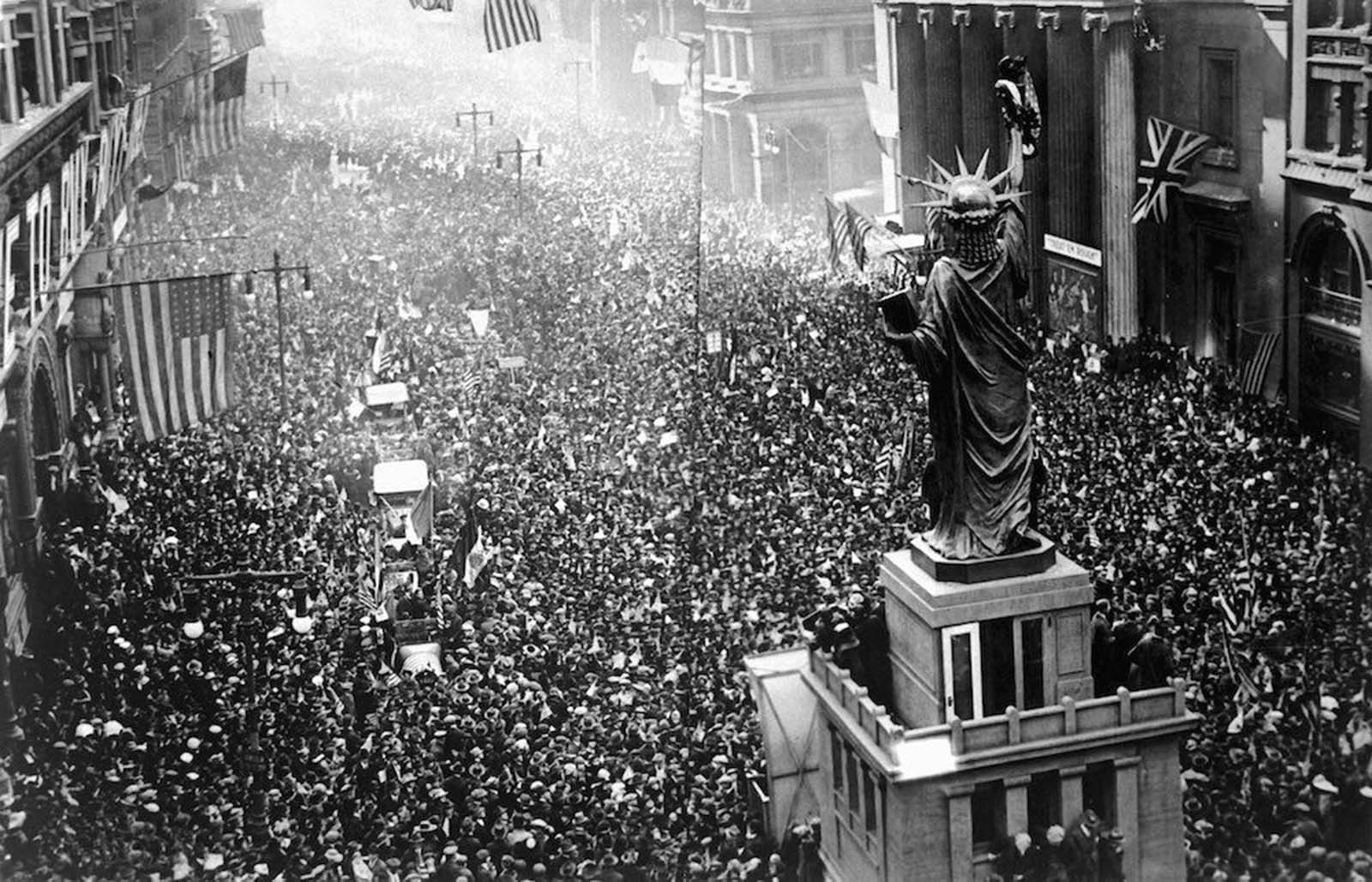 A crowd of thousands massed on Broad Street, New York, near a replica of the Statue of Liberty, to cheer as news of the armistice was announced to the public.