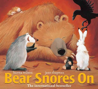 Book cover for Bear Snores On by Karma Wilson. A large golden bear is laying down sleeping while smaller animal friends are surrounding him