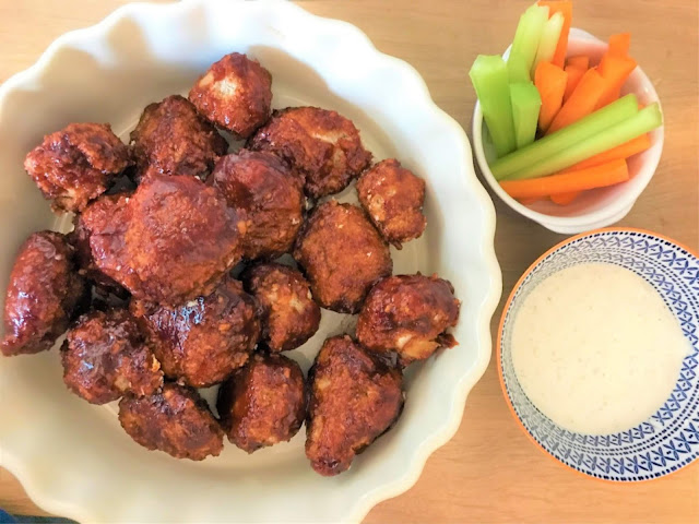 A bowl of vegan cauliflower buffalo wings with crudites and dip beside it.