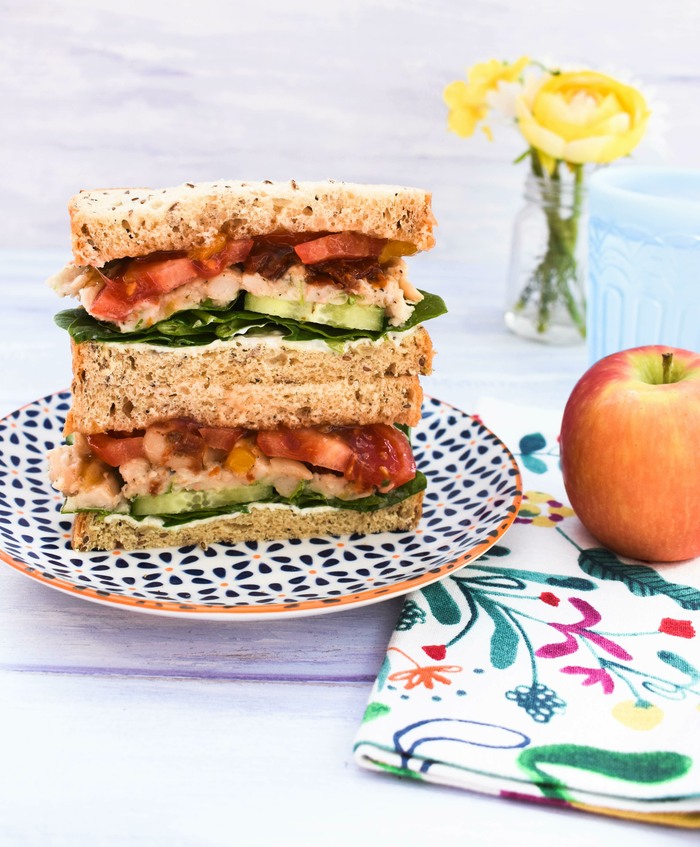 Vegan Italian Sandwich A white bean and tomato sandwich, a red apple and a glass of water