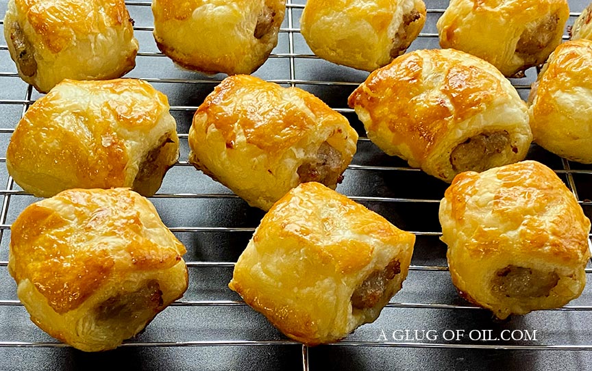 Homemade sausage rolls cooling on a wire rack.