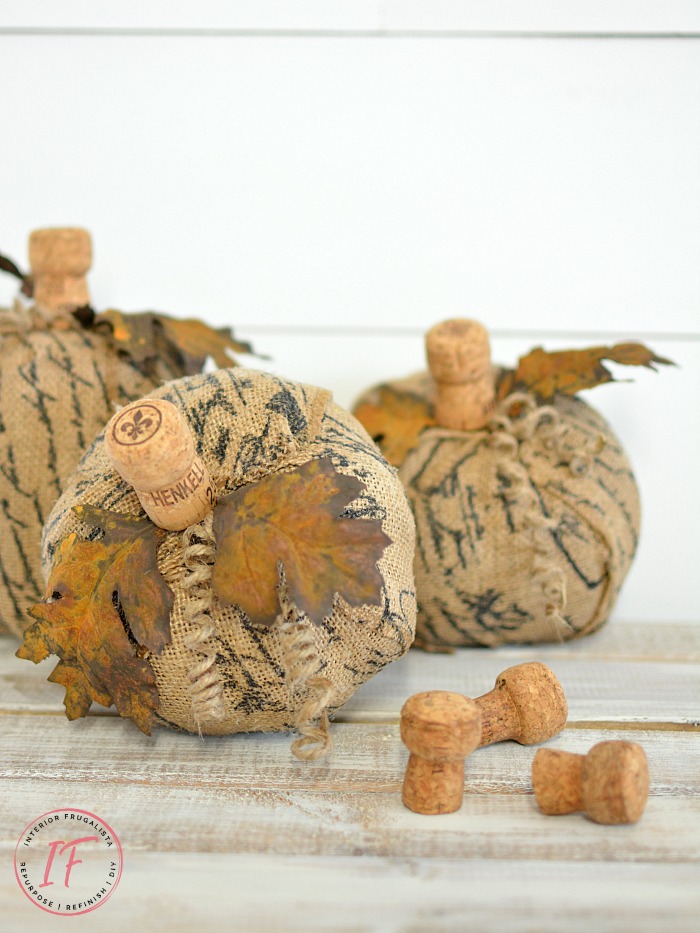 How to turn plastic dollar store pumpkins into unique French script burlap decoupage pumpkins with faux rusted iron leaves and fun wine cork stems.