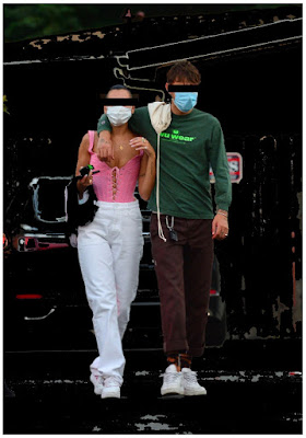 Image of a couple walking the woman wears a pink corset and white pants.